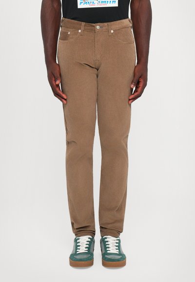 Brown corduroy pants with a slim fit, featuring five pockets, silver hardware, and worn with green suede sneakers.