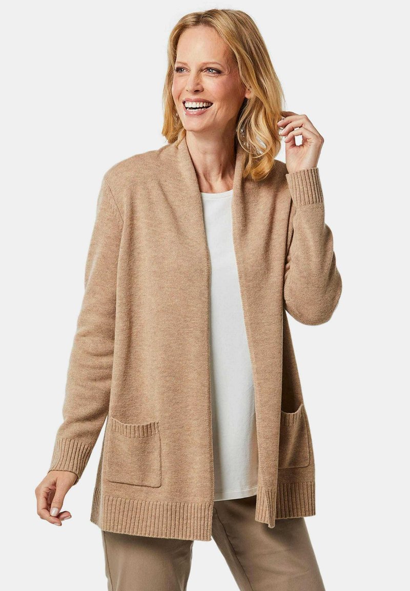 Cardigan beige en tissu doux, avec un col châle, des poignets côtelés et deux poches avant. Manches longues, coupe décontractée.