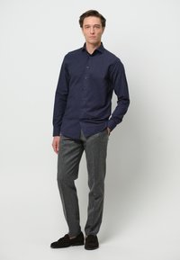 Camisa de botones de la marina con mangas largas, combinada con pantalones grises de corte ajustado y mocasines de ante oscuro. Diseño sencillo y moderno con un corte limpio.