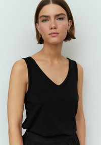 Zwarte mouwloze top met een V-halsontwerp, gemaakt van gladde stof. De silhouet is getailleerd en benadrukt de nek en schouders.