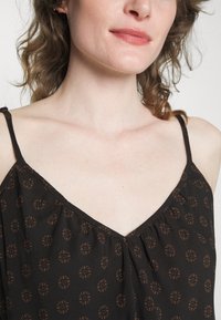 Top preto sem mangas feito de tecido leve, com um discreto padrão circular castanho, possuindo decote em V e delicadas alças finas.