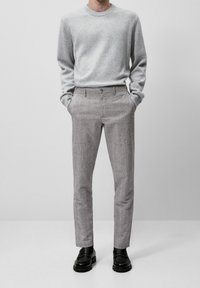 Maglione grigio lavorato a maglia con scollo rotondo, abbinato a pantaloni grigio chiaro a quadri e mocassini neri. Design semplice e aderente.