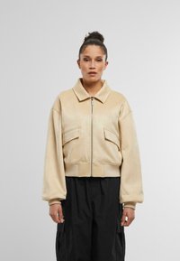 Beige skrátená bunda so zipsom vpredu, vo voľnom strihu a s dvoma prednými vreckami. Vyrobená z mäkkého materiálu s hladkou textúrou.