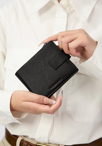 Crni kožni novčanik teksture s preklopom i zatvorenim odjeljkom na patentni zatvarač. Dizajniran s suptilnim brendingom i minimalističkom estetikom.