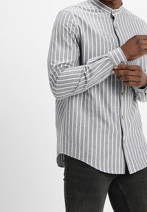 Camisa abotonada de rayas grises y blancas con cuello mao, mangas largas y un dobladillo ligeramente curvado. Combina con jeans oscuros de textura.