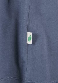 Tissu de coton bleu à texture lisse, avec une étiquette blanche portant un logo de feuille verte cousue sur la couture.