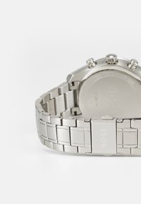 Relógio de aço inoxidável prateado com um design de bracelete ligado, apresentando uma superfície texturizada e um fecho gravado com "BOSS."