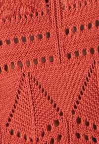 Tessuto a maglia corallo con intricati motivi di pizzo aperto, caratterizzato da piccoli fori, triangoli e punti texturizzati su tutta la superficie.