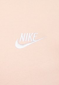 White embroidered Nike logo and swoosh on light pink fabric background.