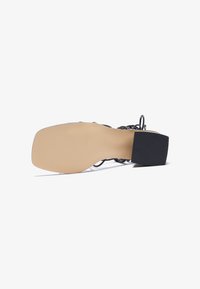 Schwarze High-Heelsandale mit einem quadratischen, strukturierten Absatz, offenem Design und einer glatten, beigen Sohle. Riemchen-Details über dem Fuß.