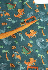 Bomuldsstof med en teal baggrund, prydet med farverige dinosaurusmønstre og palmer. Orange fleecekant med en syet label.