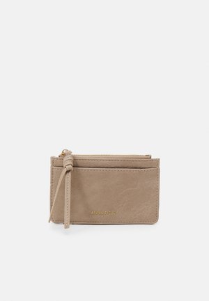 Portefeuille en similicuir beige avec une finition texturée, doté d'une fermeture éclair en haut, de plusieurs emplacements pour cartes et d'un accent à pompon sur le côté.