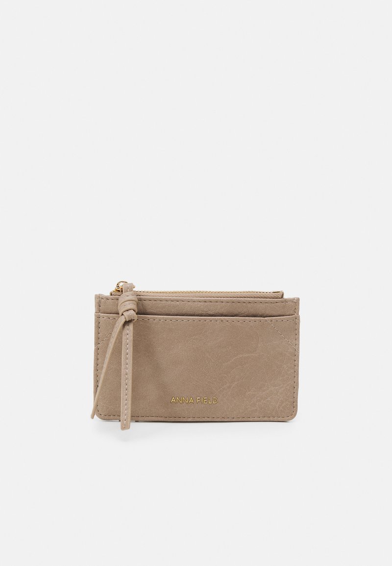 Beige faux skinnlommebok med teksturert overflate, som har en glidelås på toppen, flere kortspor og en sidepuff med dusk.
