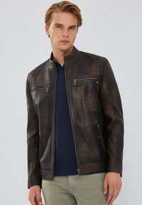 Bruine leren jas met een staande kraag, voorrits en twee borstzakken. Heeft een gestructureerde afwerking en een slim fit ontwerp.