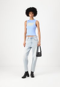 Top corto azzurro chiaro con testo grafico, abbinato a jeans straight-leg in denim chiaro. Stivaletti neri alla caviglia e una piccola borsa nera.