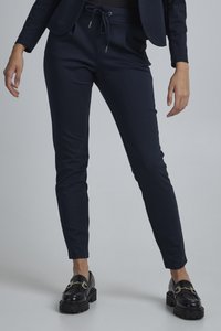 Marineblaue tapered Hosen mit elastischem Bund und Kordelzug, ausgestattet mit einer glatten Textur und zwei Seitentaschen. Kombiniert mit schwarzen Loafers.