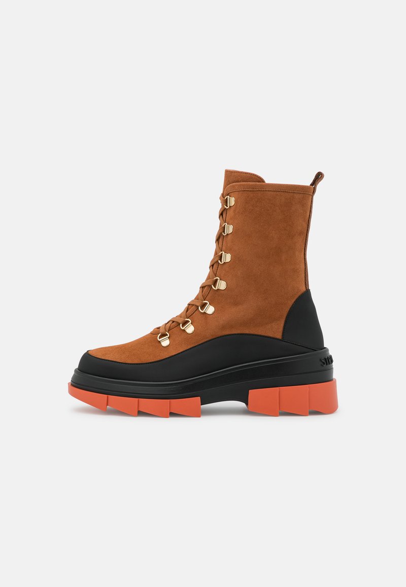 Brown suede ankle boots feature gold hardware, a black and orange chunky sole, and a lace-up design with a rear pull tab.