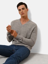 Grau, strukturierter V-Ausschnitt-Pullover mit gerippten Bündchen, kombiniert mit dunkelblauen Jeans. Das Modell sitzt vor einem neutralen Hintergrund.