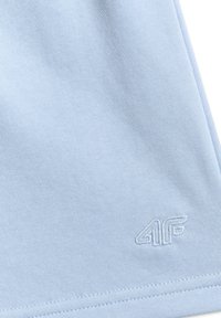 Tissu bleu clair avec un petit logo "4F" cousu près du coin inférieur et des coutures visibles le long du bord.