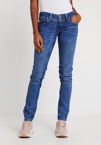 Slim-fit blå denimjeans med medelhög midja, treknapplås med gröna detaljer och minimalistiska sömfyr.