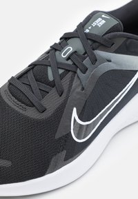 Baskets de sport noires avec un dessus en mesh, des revêtements texturés, un logo swoosh blanc et une semelle rembourrée. Les lacets sont uniformément répartis.