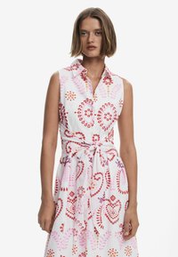 Weißes ärmelloses Kleid mit floralen Mustern in Pink, Rot und Lila. Hat einen kragenfreien Hals und ein gebundenes Taillendetail. Glatte Stofftextur.