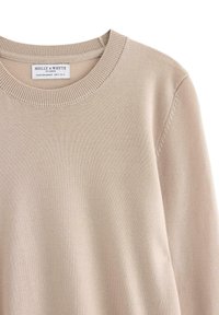Beige stickad tröja med rund halsringning, ribbad krage och slät textur. Lappen visar "Holly & Whyte by Linex."