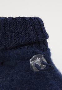 Botín de lana azul oscuro con un puño de punto acanalado. Presenta un cierre de toggle transparente y cordones planos, con una apariencia suave y texturizada.