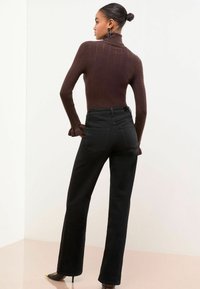 Bruine geribbelde turtleneck trui met lange mouwen, gecombineerd met zwarte high-waisted straight-leg jeans. Minimalistisch ontwerp zonder zichtbare patronen.