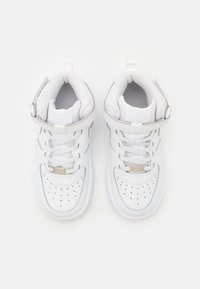 Bijele visoke tenisice od glatke kože, s perforiranim prstom i sivim akcentima. Uključuju remen oko gležnja i standardno vezivanje.