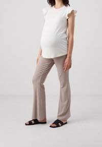 Top blanco de manga corta con acentos de volantes, combinado con pantalones acampanados de canalé en color marrón claro y sandalias negras con un diseño de tiras cruzadas.