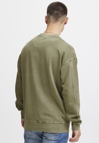 Olive green sweatshirt with a relaxed fit, ribbed cuffs and hem, and visible seam details, paired with light blue jeans.