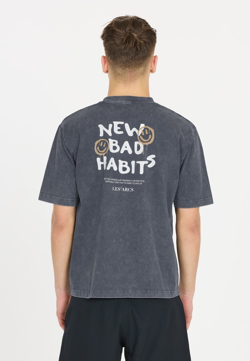 Harmaa graafinen t-paita lyhyillä hihoilla. Takana on "NEW BAD HABITS" -teksti ja hymyileviä kasvoja. Valmistettu pehmeästä, tekstuurista kankaasta.