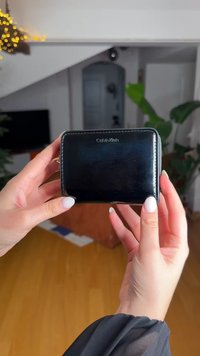 Μαύρο δερμάτινο πορτοφόλι με φερμουάρ περιμετρικά, με ασημένιο λογότυπο Calvin Klein και λεία υφή. Ορατά χέρια που κρατούν το πορτοφόλι.