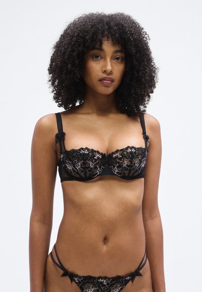 Black lace bra with floral embroidery, underwire support, and satin straps. Includes matching lace thong with adjustable straps and bows.
