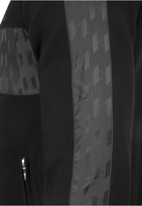 Czarna bluza z teksturowanym czarnym panelem i geometrycznym wzorem na rękawach. Posiada kieszenie boczne na zamek.