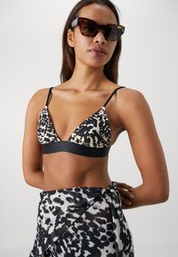 Driehoek bralette in dierenprint met beige, zwart en bruin. Heeft dunne verstelbare bandjes en een zwarte elastische band.
