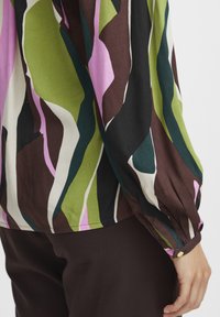 Langarmbluse mit einem mehrfarbigen abstrakten Muster in Grün, Pink, Braun und Schwarz; verfügt über einen knöpfbaren Manschette und eine weiche Stofftextur.