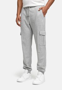 Grey sweatpants made of soft fabric, featuring side pockets and a tapered ankle design. Worn with white sneakers.