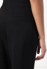 Black sweatpants featuring a smooth fabric texture, an elastic waistband, and a small back pocket with a flat seam detail.