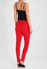 Pantalons rouges à taille élastique avec coupe ajustée, associés à un haut sans manches noir. Texture lisse, peu de détails et design uni.