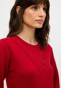 Czerwona sweter z okrągłym dekoltem i wycięciem w kształcie litery V. Wykonany z miękkiego materiału, ma gładką teksturę i dopasowany krój.