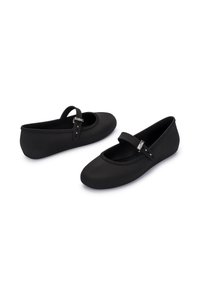 Bailarinas negras de material suave, con puntera redonda y una correa con herrajes metálicos. Diseño suave y flexible.