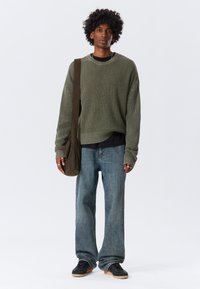 Green knitted sweater with a textured pattern, layered over a black shirt. Light blue denim jeans and black sneakers with gum soles. Brown shoulder bag.