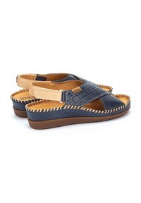 Sandalias de cuero azul marino con diseño perforado, acentos beige, detalles cosidos y plantilla acolchada con un tacón bajo.