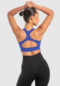 Blå sportbh med racerback-design och utskärningar, tillsammans med högmidjade svarta leggings. Slät textur, åtsittande stil.