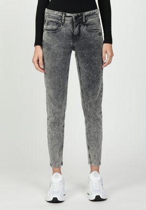 Graue Denim-Jeans mit einem verblassten Finish, schmaler Passform, Fünf-Taschen-Design und kontrastierenden Nähten, kombiniert mit weißen Sportschuhen.