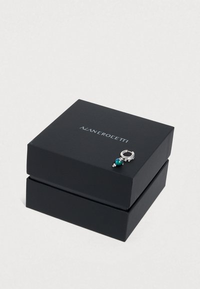 Μαύρο κουτί κοσμημάτων με γυαλιστερό φινίρισμα· διαθέτει ασημένιο κούμπωμα διακοσμημένο με σκούρο πράσινο λίθο· κείμενο "ALAN ROLETTI" στην κορυφή.