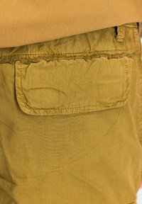 Khaki šortky s našitou priestrannou kapsou so strapcami, vyrobené z mäkkej látky s jemnou textúrou a voľným strihom v oblasti pásu.