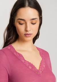 Top a maniche lunghe rosa con una trama a coste e scollatura a V rifinita in pizzo. Il pizzo presenta motivi floreali lungo il neckline.